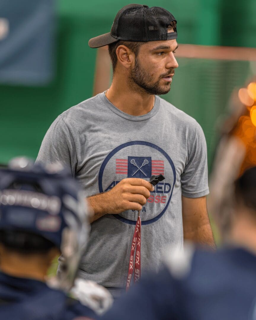 Man in cap holding lacrosse stick indoors.