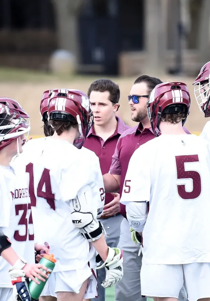 A group of lacrosse players gathered around a coach.